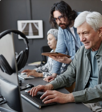 A group of people is gathered around a computer, with one person actively typing on the keyboard while another holds a tablet, seemingly engaged in a collaborative activity.